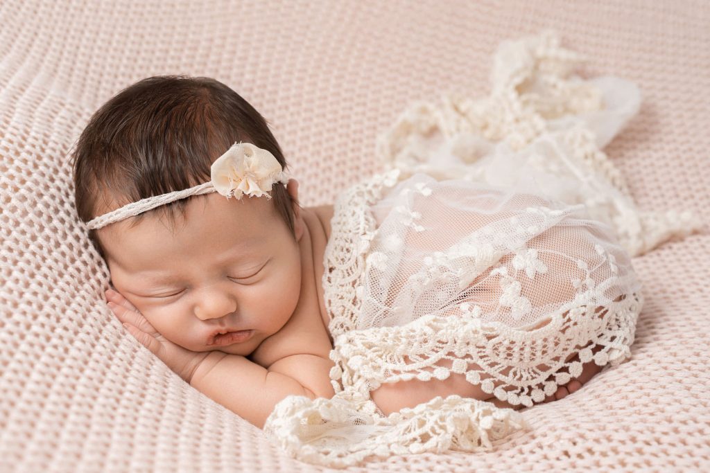 das babygirl in zarter spitze eingewickelt, bäuchlings schlafend auf einer rosafarbenen decke