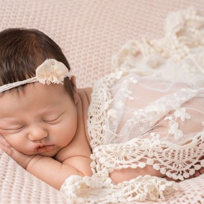 beim babyshooting ist das babygirl in zarter spitze eingewickelt, bäuchlings schlafend auf einer rosafarbenen decke