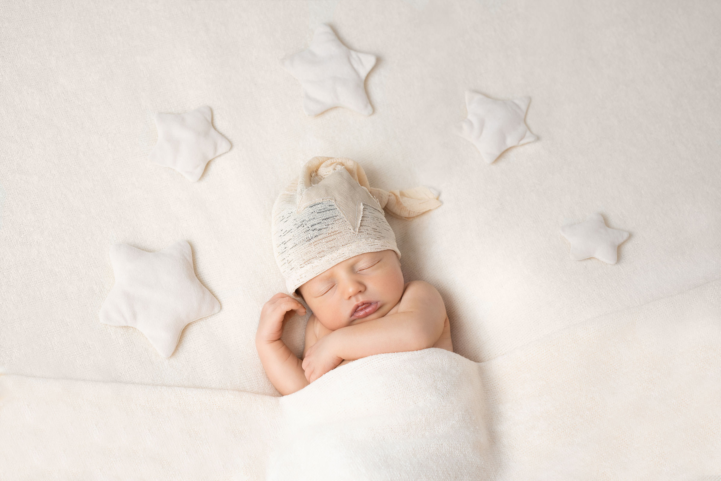 Babyfotografie Bergisch Gladbach. mit heller decke zugedecktes baby mit zipfelmütze, eingerahmt von sternen