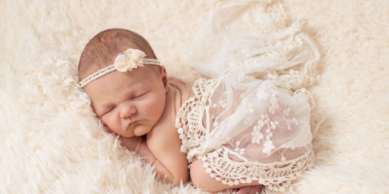 das babygirl in zarter spitze eingewickelt, bäuchlings schlafend auf einer rosafarbenen decke